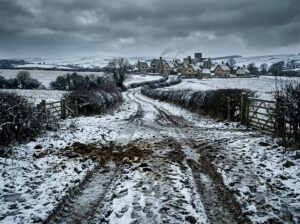 A muddy, snow-speckled dirt road leading toward a winter village on the human side of the wall in A Court of Thorns and Roses.